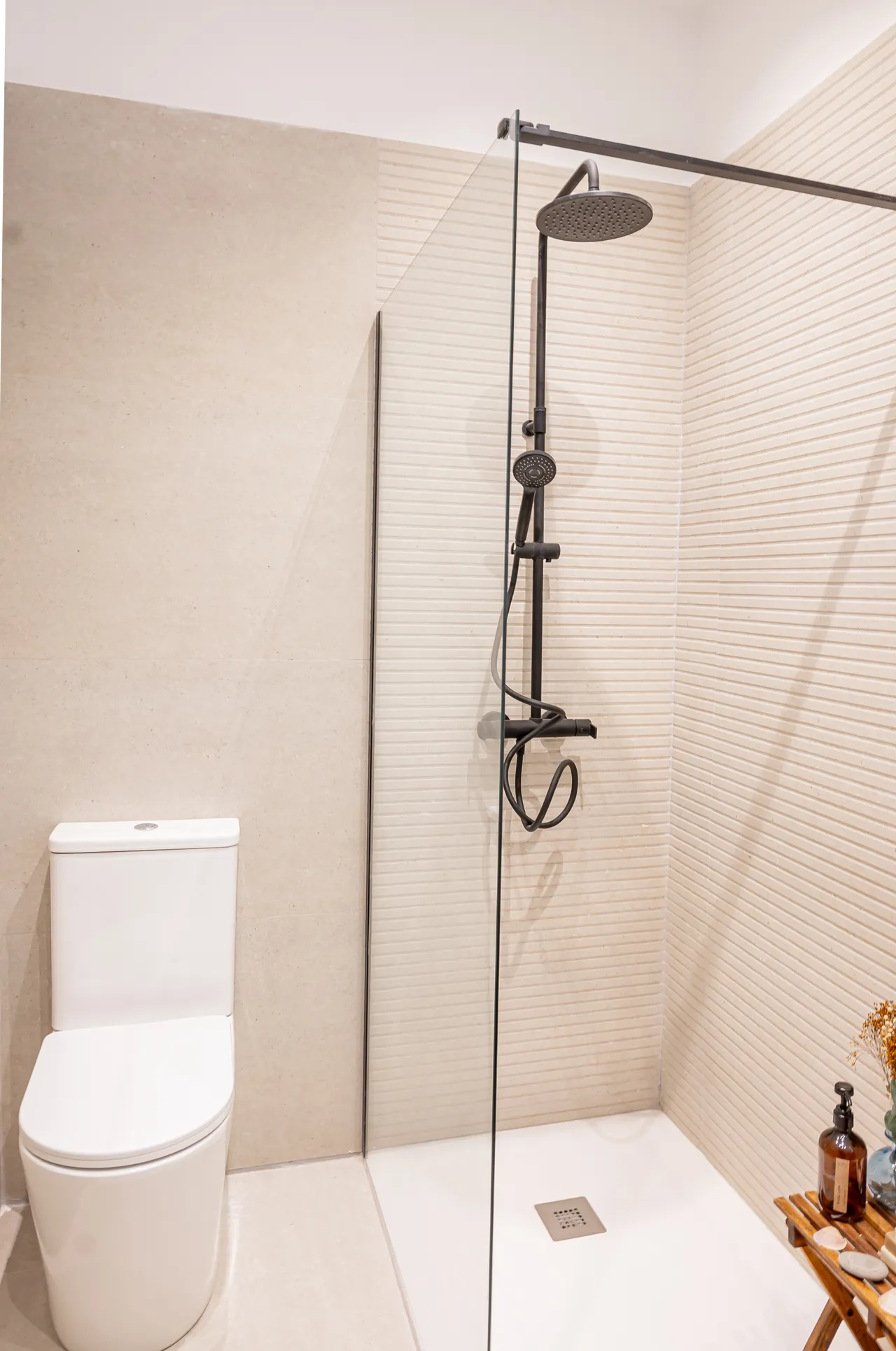 Baño reformado con ducha de obra, azulejo estriado y grifería negra mate.
