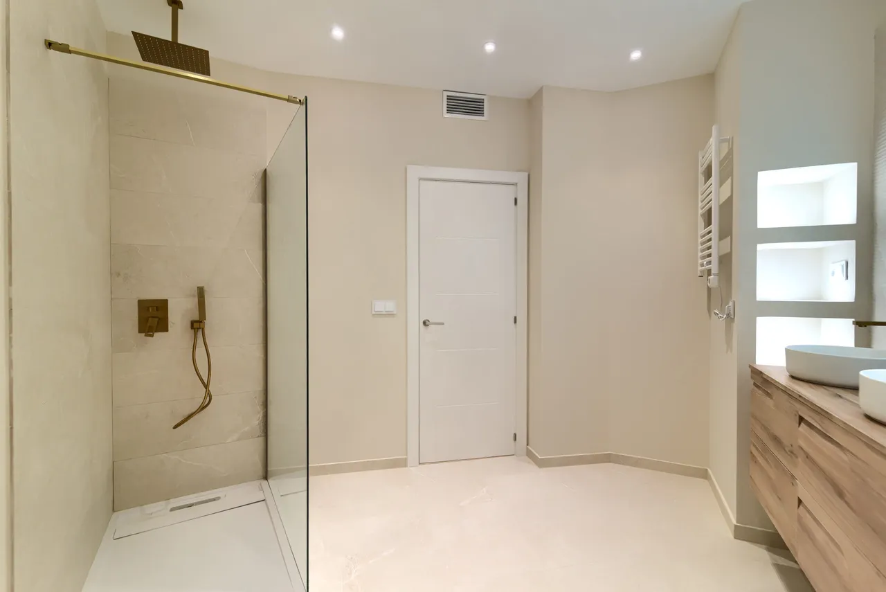 Baño reformado con plato de ducha, grifería de latón y mueble de madera natural.