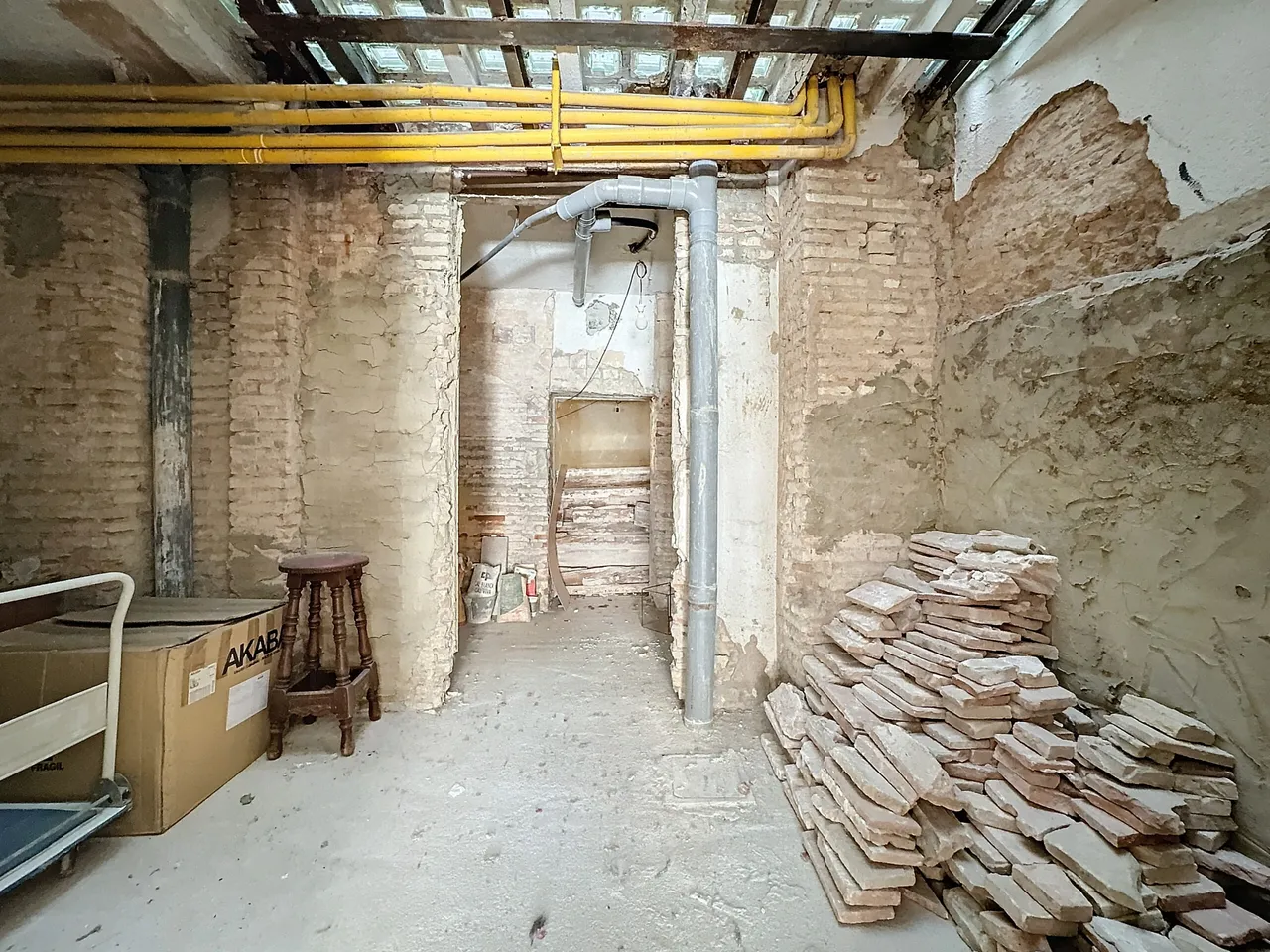 Interior de un bajo en reforma con el ladrillo desnudo a la vista, las instalaciones vistas y material acopiado.