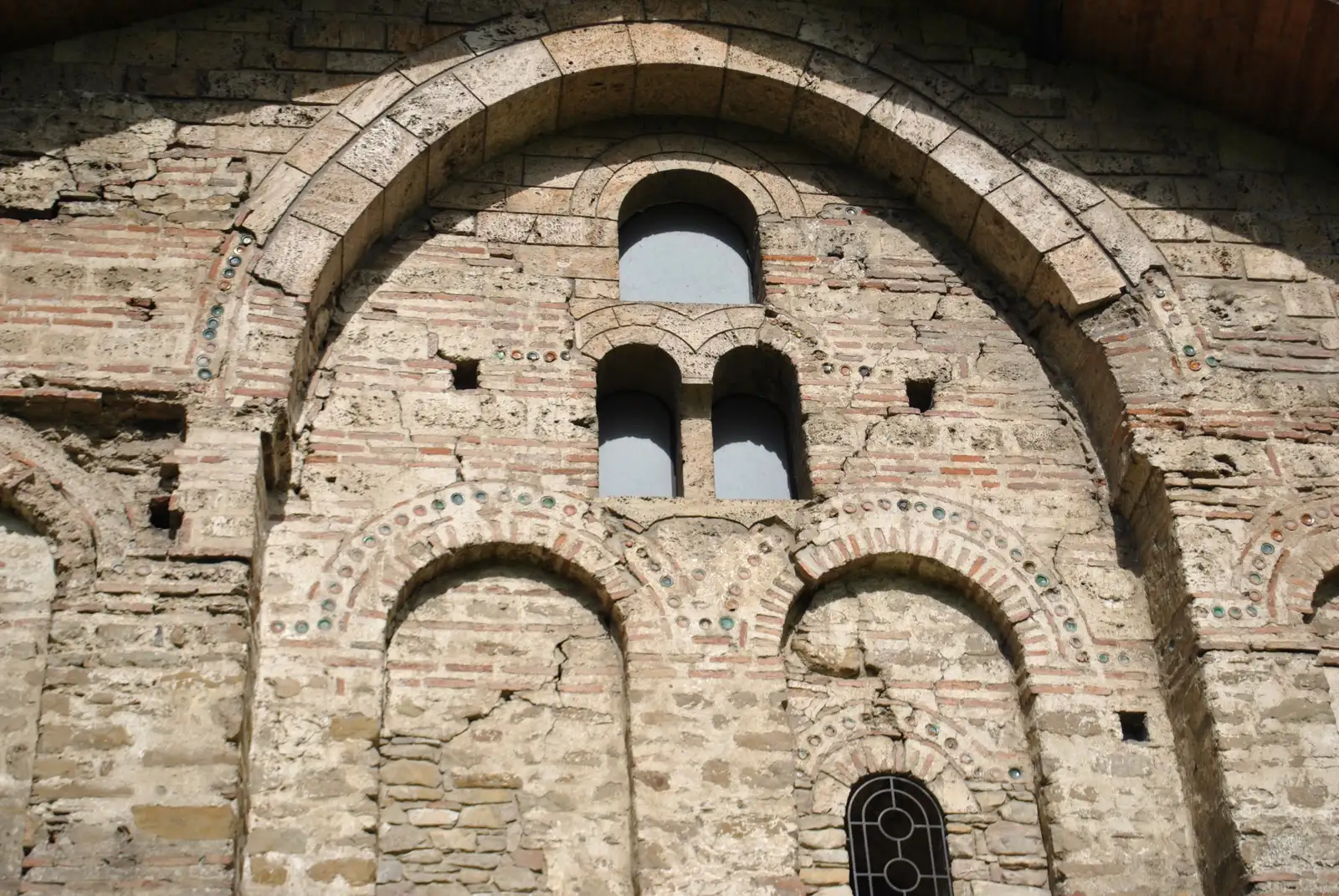Fachada de fábrica de ladrillo y piedra vista de frente, con un gran arco de medio punto que enmarca tres vanos superiores y, bajo él, dos arcos ciegos y un ventanuco inferior con vidrios emplomados.